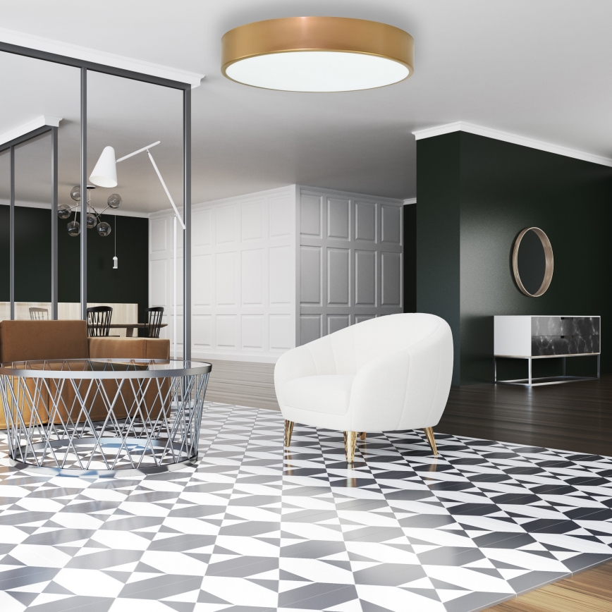 Biely kreslový nábytok stojí na čierno-bielej dlažbe. Nad ním je kruhové stropné svietidlo. Prostredie tvorí moderný interiér s tmavozelenou stenou.