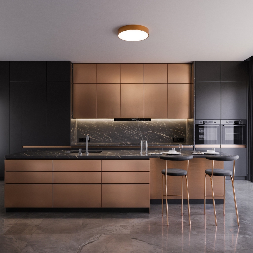 Kuchynská linka s medenými skrinkami a čiernou doskou sa nachádza v moderne zariadenej kuchyni s tmavými stenami a dlažbou. Na ostrove sú umiestnené tri vysoké stoličky.