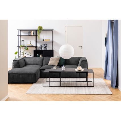 Sivá rohová sedačka s vankúšmi stojí v obývacej izbe. Pred ňou je súprava troch prepojených konferenčných stolíkov s čiernym rámom. V pozadí je polica a biela lampa.