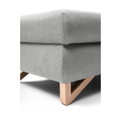 Šedá čalúnená taburetka s drevenými nohami v tvare písmena X stojí na bielom pozadí.