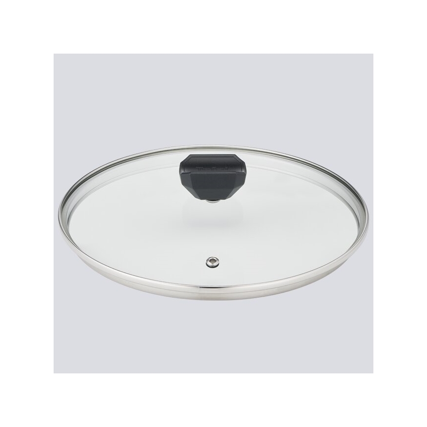 Sklenený poklop s nerezovým okrajom a čiernou úchytkou leží na svetlom podklade. Poklop je umiestnený vodorovne.