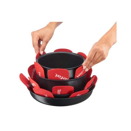 Dve ruky ukladajú červené podložky Tefal medzi dve čierne panvice. Panvice sú stohované na sebe. Podložky sú umiestnené okolo okrajov hornej panvice.
