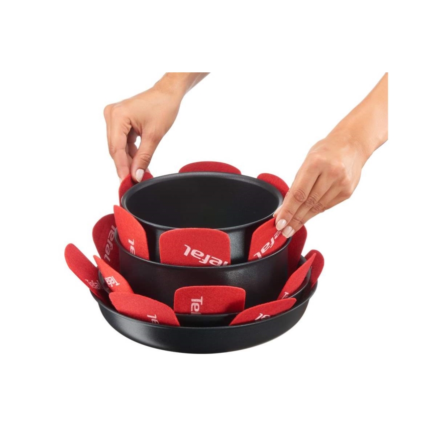 Dve ruky ukladajú červené podložky Tefal medzi dve čierne panvice. Panvice sú stohované na sebe. Podložky sú umiestnené okolo okrajov hornej panvice.
