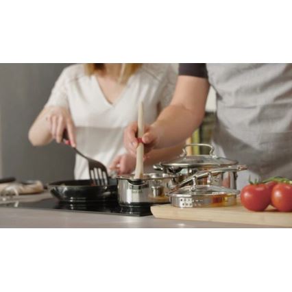 Dvojica varí v kuchyni. Muž mieša drevenou varechou v hrnci, žena mieša špachtľou v panvici. Na indukčnej doske sú rozložené hrnce, panvica a miska s paradajkami.
