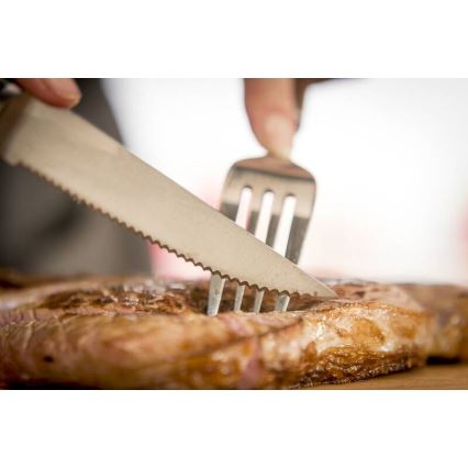 Steak sa krája nožom a vidličkou. Na drevenom podklade.
