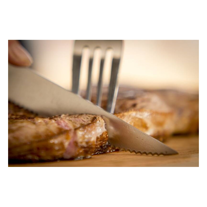 Nôž krája opečený steak na drevenej doske. Vidlička je blízko.