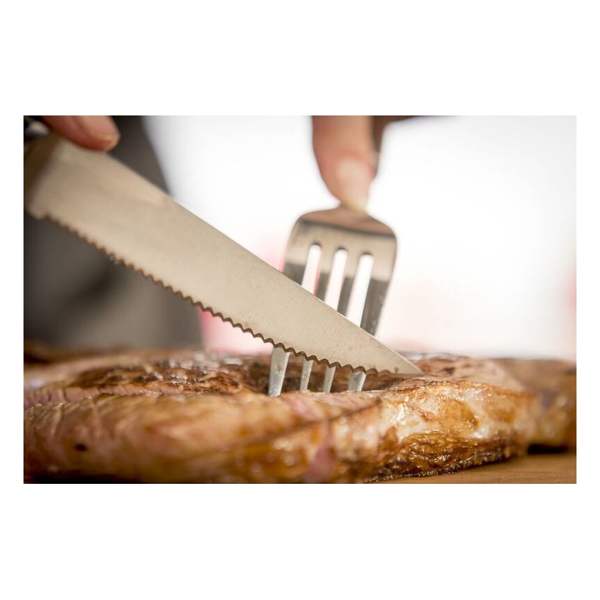 Steak sa krája nožom a vidličkou. Na drevenom podklade.