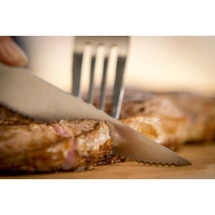 Nôž krája opečený steak na drevenej doske. Vidlička je blízko.