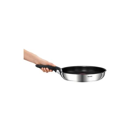 Ruka drží nepriľnavú panvicu Tefal s nerezovou konštrukciou a čiernym dnom. Panvica je držaná za ergonomickú rukoväť. Panvica je umiestnená pred bielym pozadím.