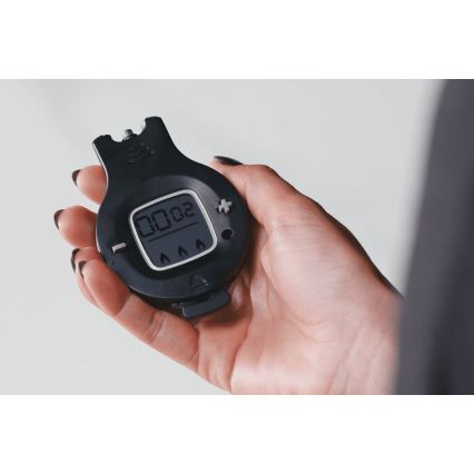 Čierny digitálny časovač drží ruka. Displej zobrazuje 00:02. Časovač má tlačidlá a symboly plameňov.