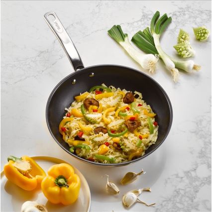 Wok s cestovinovou zmesou a zeleninou, vrátane paprík a romanesco, sa nachádza na mramorovom povrchu spolu s cesnakom a jarnou cibuľkou.