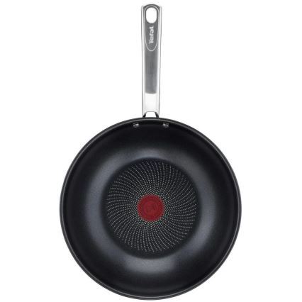 Wok Tefal s kovovou rukoväťou je zobrazený zhora. Jeho vnútorná časť je tmavá s bodkovaným vzorom vychádzajúcim zo stredu, kde je viditeľné červené logo.