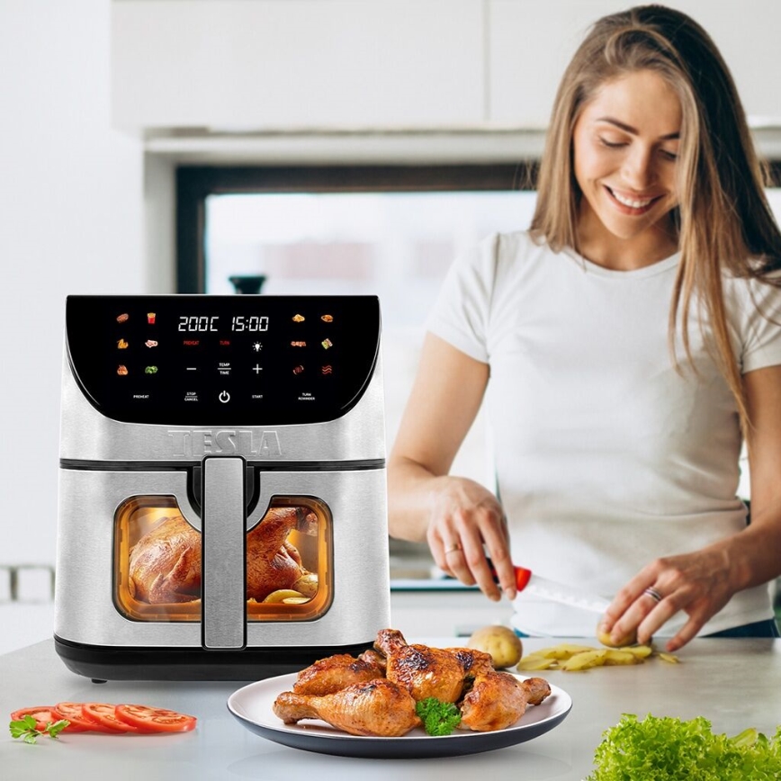 Air fryer Tesla pripravuje kurča. Žena krája zeleninu pri kuchynskej linke. Na displeji air fryeru svieti 200°C 15:00.