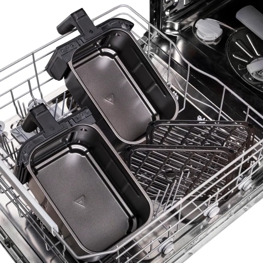 Dve tmavé pekáče a dva rošty sa umývajú v umývačke riadu. Pekáče sú umiestnené vertikálne, rošty horizontálne. Umývačka je z nerezovej ocele.