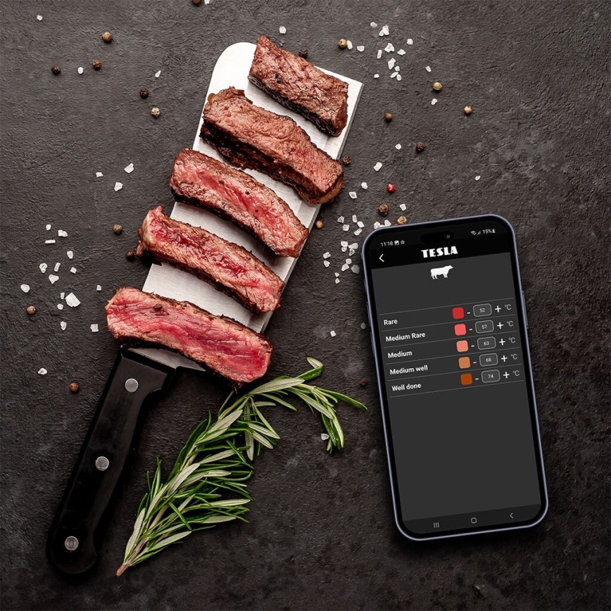 Na tmavej doske ležia narezané steaky. Vedľa nich je mobilný telefón s aplikáciou Tesla zobrazujúcou stupnicu prepečenia mäsa: Rare (45-50°C), Medium Rare (50-57°C), Medium (57-63°C), Medium well (63-68°C), Well done (68-71°C).