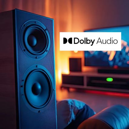 Reproduktor prehráva zvuk v domácom prostredí. Na pozadí je televízor a nábytok. Na obrázku je tiež logo „Dolby Audio“.