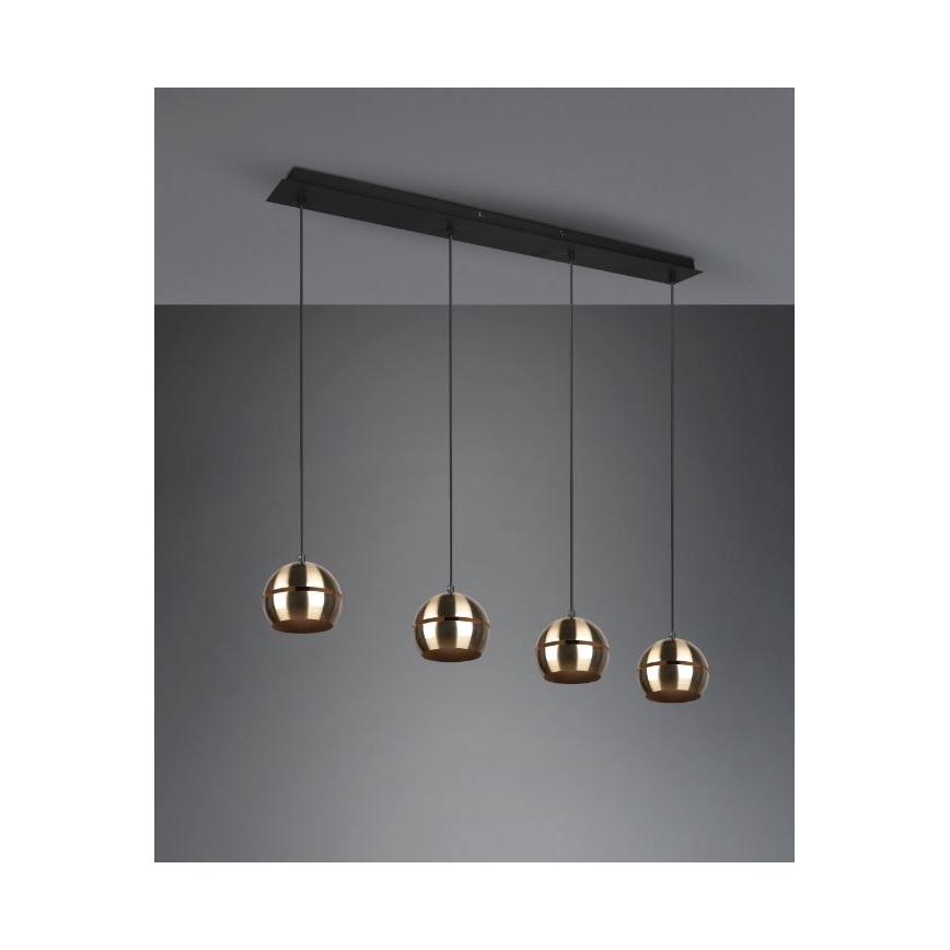 Štvorramenné závesné svietidlo visí zo stropnej lišty. Štyri zlaté guľové tienidlá sú zavesené na čiernych kábloch. Lišta je čierna a pripevnená k stropu.
