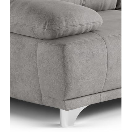 Sivá sedačka s mäkkým čalúnením stojí na bielych nožičkách. Je zobrazená detailná časť bočnej strany a opierky.