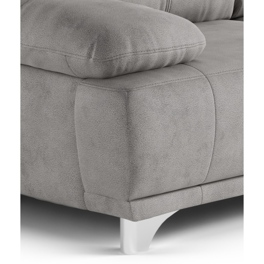 Sivá sedačka s mäkkým čalúnením stojí na bielych nožičkách. Je zobrazená detailná časť bočnej strany a opierky.