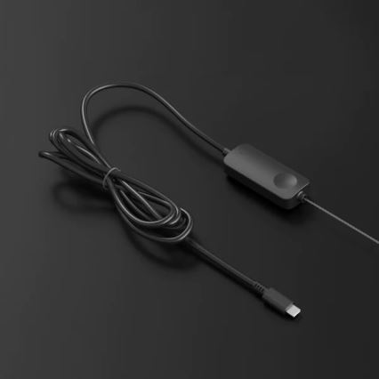 Čierny kábel s USB-C konektorom je pripojený k malej čiernej krabičke s tlačidlom. Krabica je umiestnená na tmavosivej ploche.