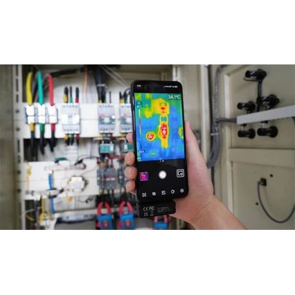 Mobilný telefón sníma termovíziu elektrického rozvádzača. Na displeji je zobrazená teplotná mapa s hodnotami od 28.5 °C do 40.7 °C a maximálnou teplotou 34.1 °C. Rozvádzač obsahuje rôzne elektrické komponenty a káble.