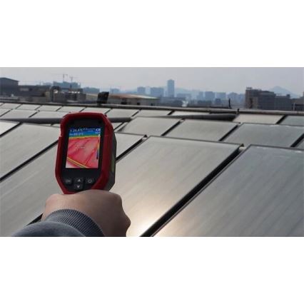 Termokamera sníma teplotu solárnych panelov na streche budovy s výhľadom na mesto. Displej zobrazuje teplotu 26,4 °C a 55,0 °C.