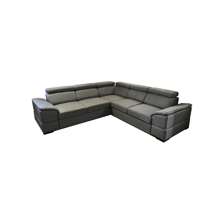 Rohová sedačka sivomodrej farby stojí v obývacej izbe s drevenou podlahou. Pred ňou je sklenený konferenčný stolík na koberci s geometrickým vzorom. V pozadí je čiastočne viditeľná moderná kuchyňa.