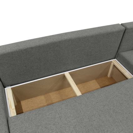 Rozkladacia sedačka s otvoreným úložným priestorom rozdeleným drevenými priečkami. Úložný priestor je pod sedákom, čalúnenie je sivé.