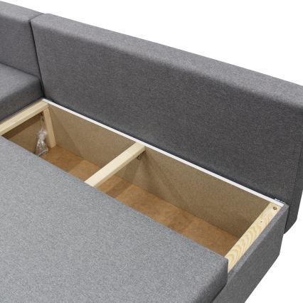 Rohový gauč s otvoreným úložným priestorom. Vnútorná konštrukcia z dreva je viditeľná. Sivá látková poťah.