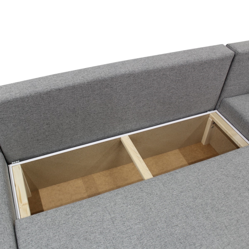 Rozkladacia sedačka odhaľuje úložný priestor. Sedačka je sivá, látková, s drevenou konštrukciou úložného priestoru, rozdeleného na dve časti.
