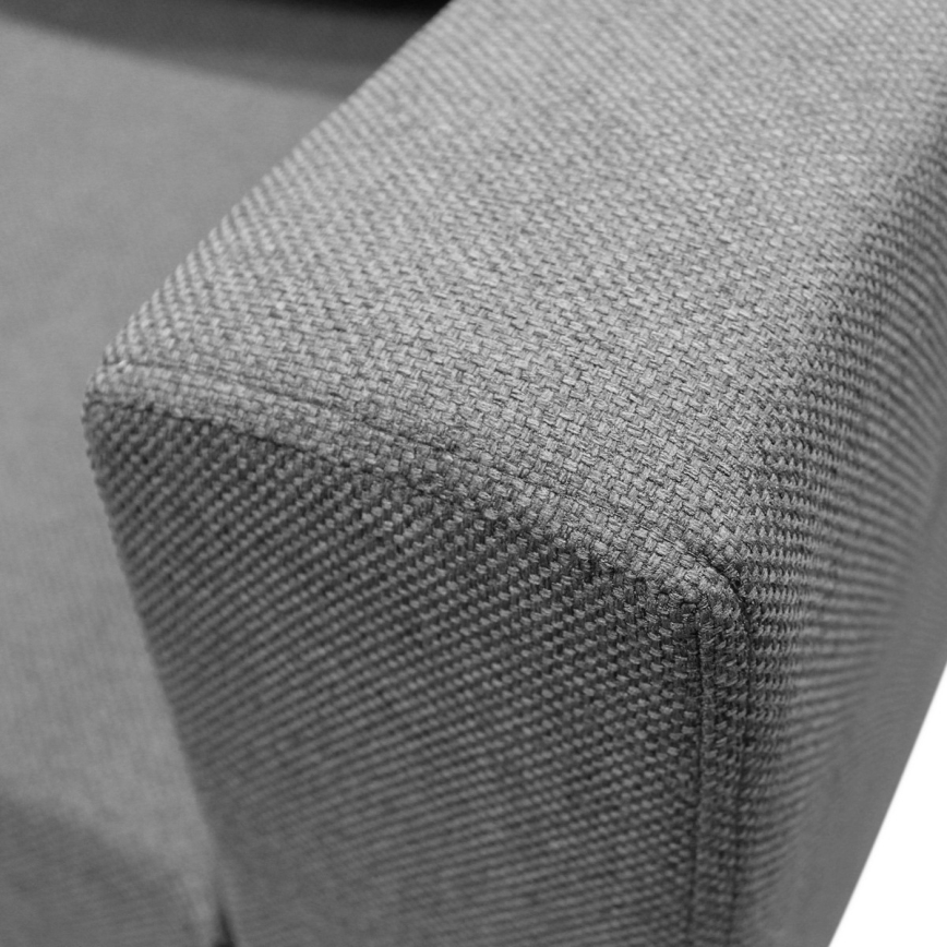 Rohová sedačka sivomodrej farby s viacerými vankúšmi je umiestnená na čiernom podstavci pred bielym pozadím. Sedačka je zobrazená zo zadnej strany.