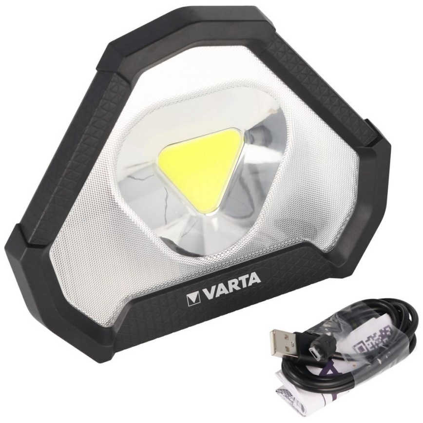Prenositelná LED pracovná lampa VARTA s trojuholníkovým tvarom a integrovanou LED diódou, svieti. K lampe patrí USB kábel na nabíjanie.