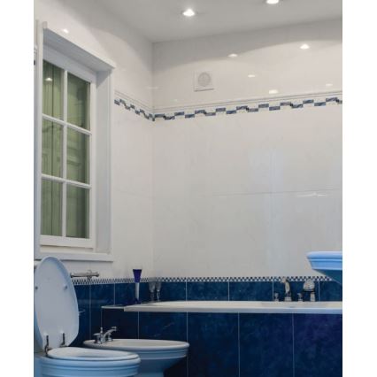 Kúpeľňa s bielymi stenami a modrým obkladom okolo vane. V kúpeľni je WC, bidet a vaňa. Na strope sú zabudované svetlá.