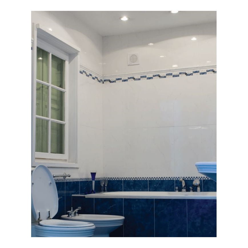 Kúpeľňa s bielymi stenami a modrým obkladom okolo vane. V kúpeľni je WC, bidet a vaňa. Na strope sú zabudované svetlá.