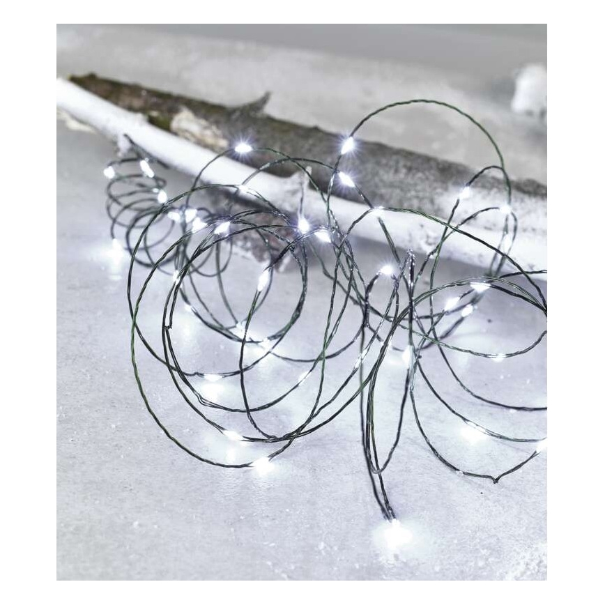 Svetelný retiazok s bielymi LED diódami je stočený na snehu. Tenký, tmavý kábel s mnohými malými svetlami leží na svetlom drevenom kuse dreva.