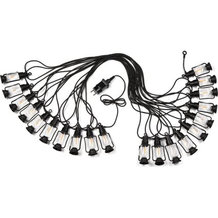 Svetelný reťaz s pätnástimi malými čiernymi lampášikmi s teplým svetlom je zapojený do elektrickej siete. Lampáše visia na čiernom kábli na bielom pozadí.