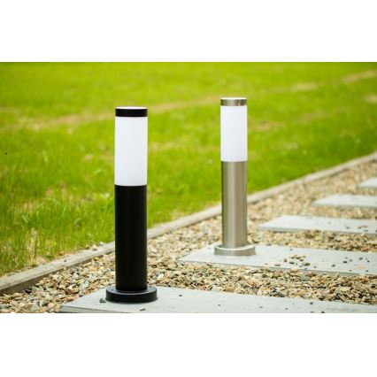 Dve záhradné lampy stoja na kamenistej cestičke vedľa trávnika. Jedna lampa je čierna, druhá nerezová. Obe majú bielu difúznu časť na vrchu.