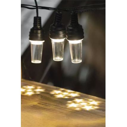 Svetelná reťaz s tromi svietiacimi valcovými žiarovkami zavesenými na čiernom kábli, vytvára hviezdny vzor svetla na drevenom povrchu pod sebou.