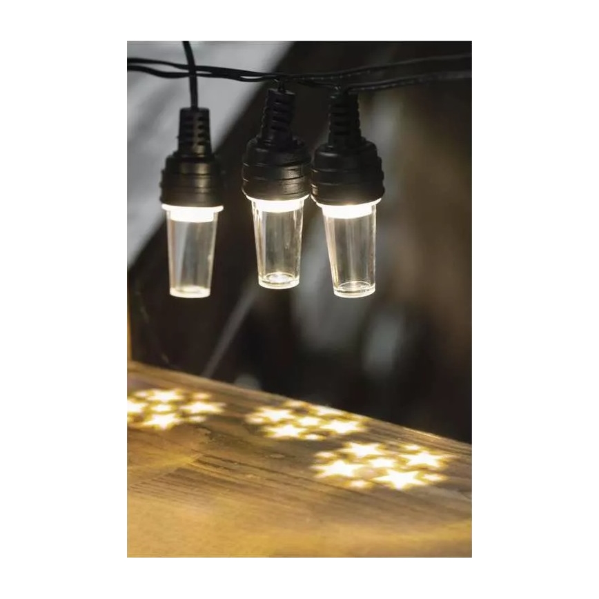 Svetelná reťaz s tromi svietiacimi valcovými žiarovkami zavesenými na čiernom kábli, vytvára hviezdny vzor svetla na drevenom povrchu pod sebou.