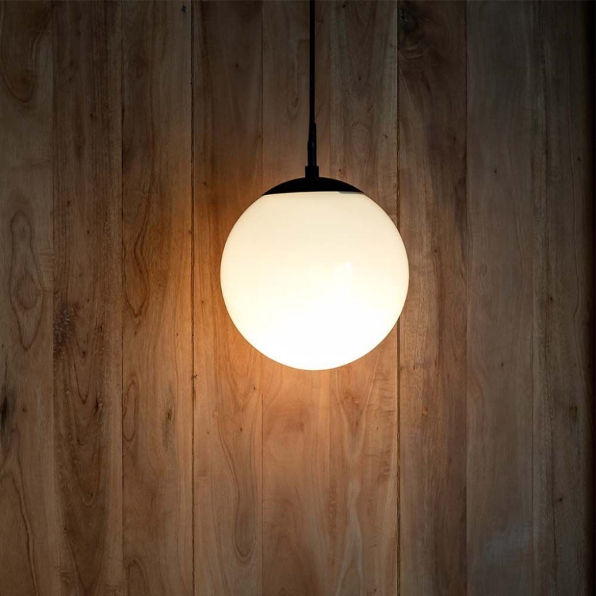 Guľová lampa svieti. Je zavesená na čiernom káble pred drevenou stenou.