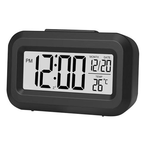 Digitálny budík zobrazuje čas 12:00 PM, dátum 12/20 a teplotu 26 °C. Je čierny, obdĺžnikového tvaru a stojí na bielom pozadí.