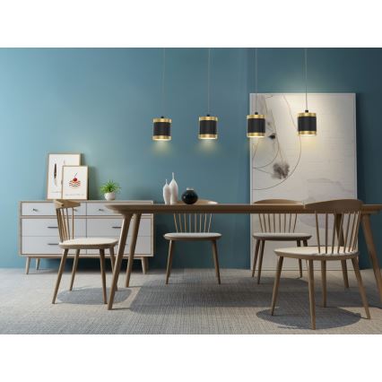 Štyri závesné svietidlá svietia nad jedálenským stolom v jedálni. Svietidlá sú valcovité, čierne s pozláteným lemom. Stôl je obklopený drevenými stoličkami. Steny sú tmavomodré.