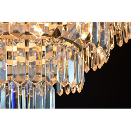 Krištáľový luster visí v tme. Je zložený z mnohých visiacich, hranolových krištáľov, ktoré vytvárajú viacvrstvový efekt. Svetlo presvitá cez krištále a vytvára dúhové odlesky.