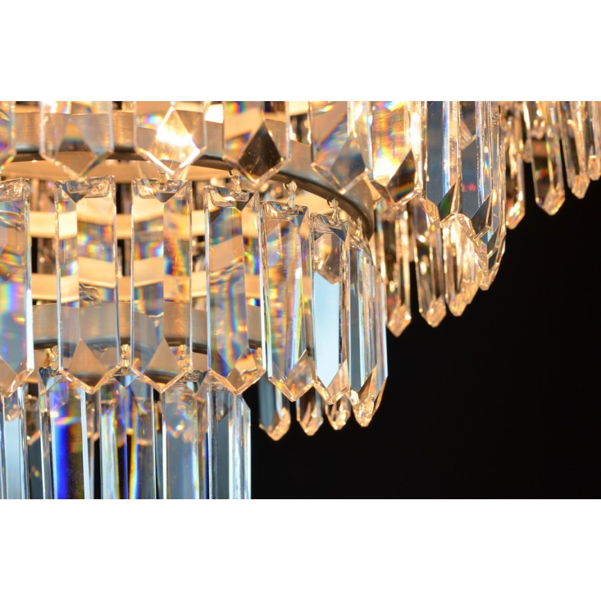 Krištáľový luster visí v tme. Je zložený z mnohých visiacich, hranolových krištáľov, ktoré vytvárajú viacvrstvový efekt. Svetlo presvitá cez krištále a vytvára dúhové odlesky.
