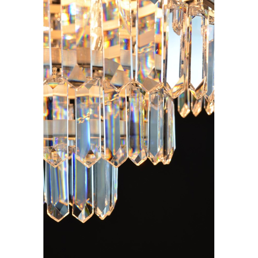 Krištáľový luster s mnohými visiacimi hranolmi z krištáľového skla, ktoré sa lesknú na tmavom pozadí.