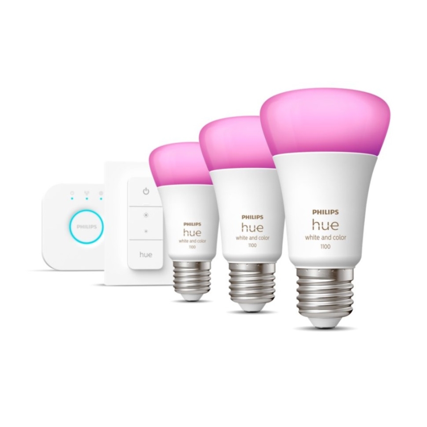 Tri inteligentné žiarovky Philips Hue, svietiace ružovo, sú umiestnené vedľa seba. Súčasťou sady je aj diaľkový ovládač a malá základňa. Na žiarovkách je uvedené: PHILIPS hue white and color 1100.
