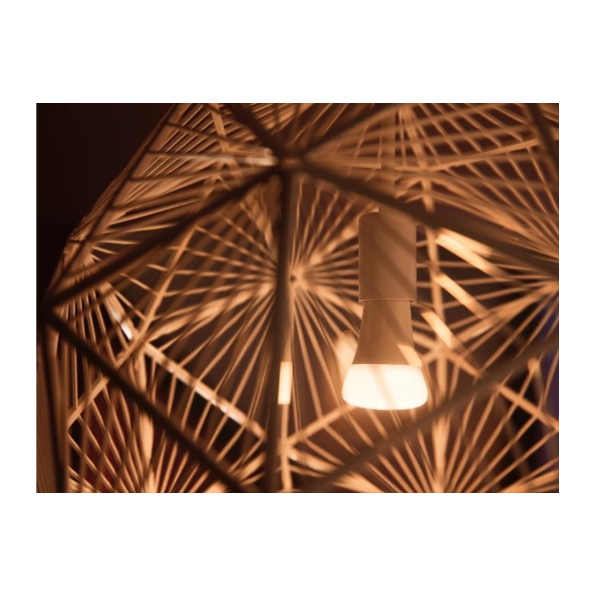 Svetlo svieti vnútri geometrickej lampy z prútia. Žiarovka je umiestnená v strede, obklopená prepletenými prútmi. Konštrukcia lampy je viacuholníková a pripomína kôš.