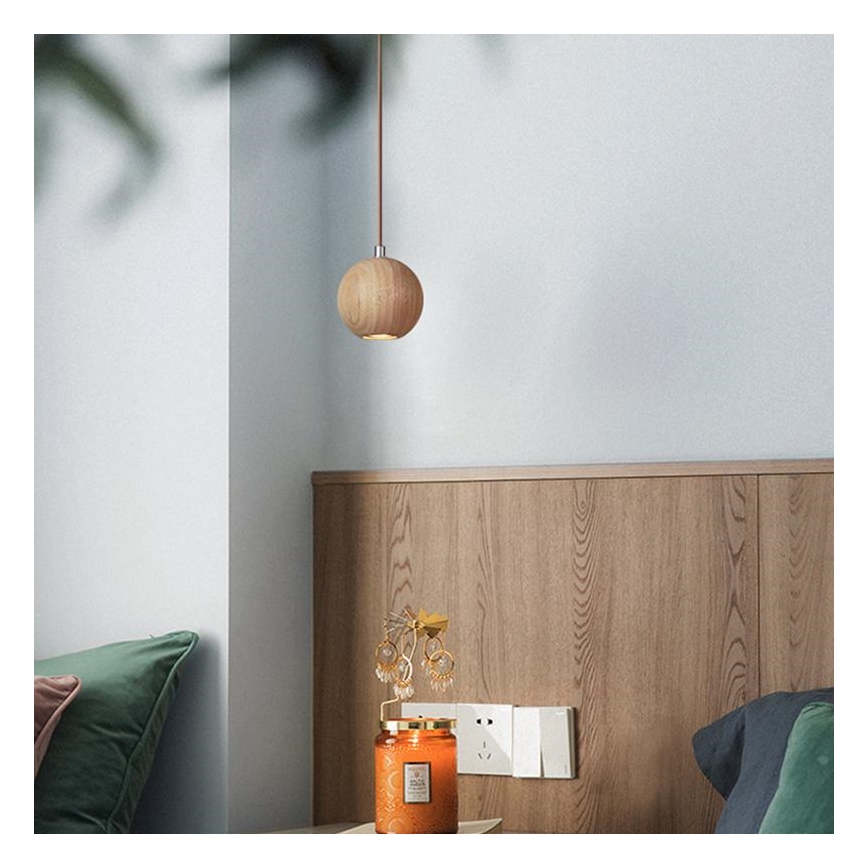 Drevené guľové svietidlo visí zo stropu. Nachádza sa v spálni pri posteli s dreveným čelom, na nočnom stolíku je sviečka a stojan na náušnice.