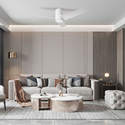 Biely stropný ventilátor s tromi lopatkami rotuje v moderne zariadenej obývacej izbe s rozsiahlou pohovkou a dvoma konferenčnými stolíkmi. Pohovka je svetlá, s niekoľkými vankúšmi. Izba má neutrálne farby stien a drevené panely.