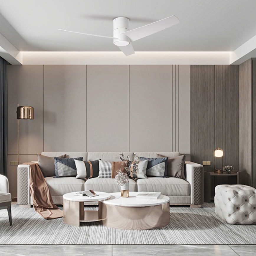 Biely stropný ventilátor s tromi lopatkami rotuje v moderne zariadenej obývacej izbe s rozsiahlou pohovkou a dvoma konferenčnými stolíkmi. Pohovka je svetlá, s niekoľkými vankúšmi. Izba má neutrálne farby stien a drevené panely.